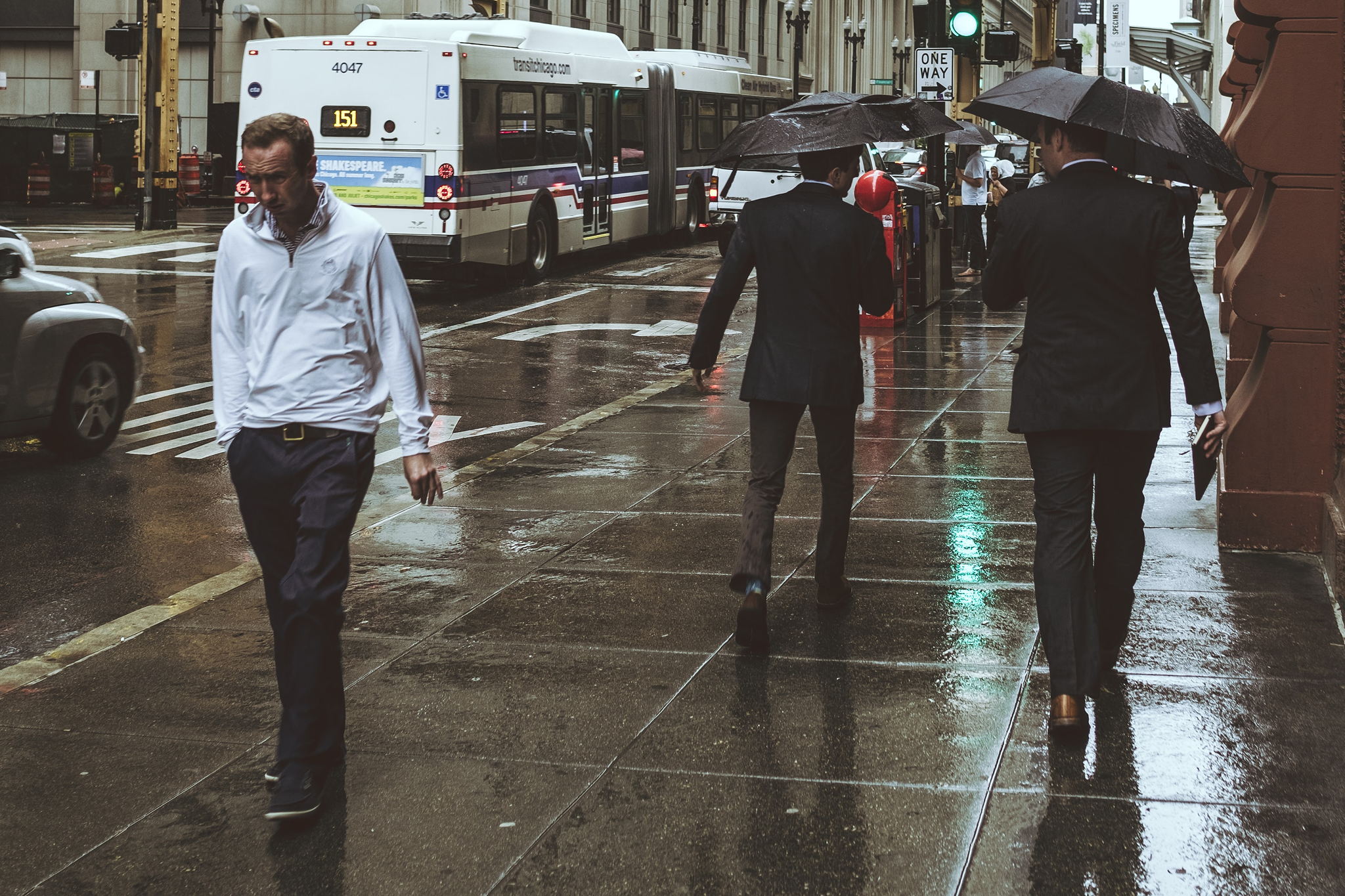 A man walks down the sidewalk squinting into the rain.
