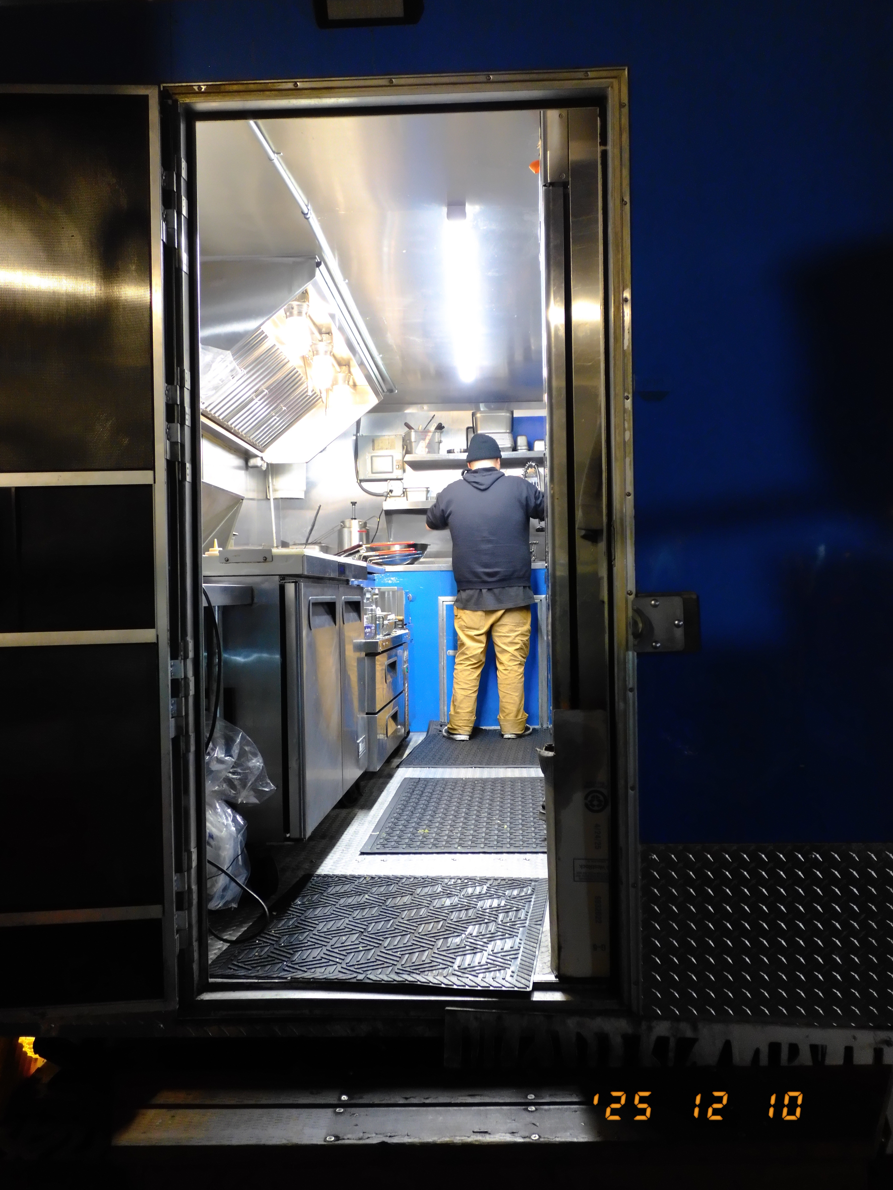 A person is working inside a food cart kitchen, viewed through an open door.