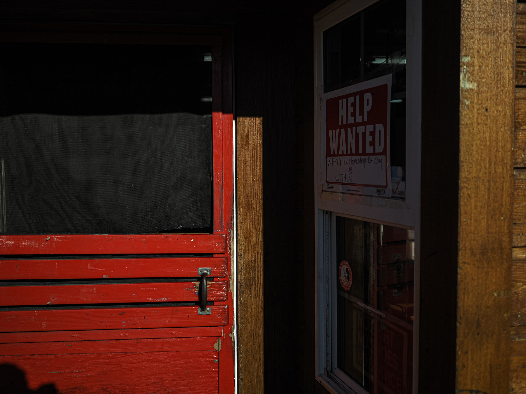 A red door and window display a Help Wanted sign in a dimly lit rustic setting.